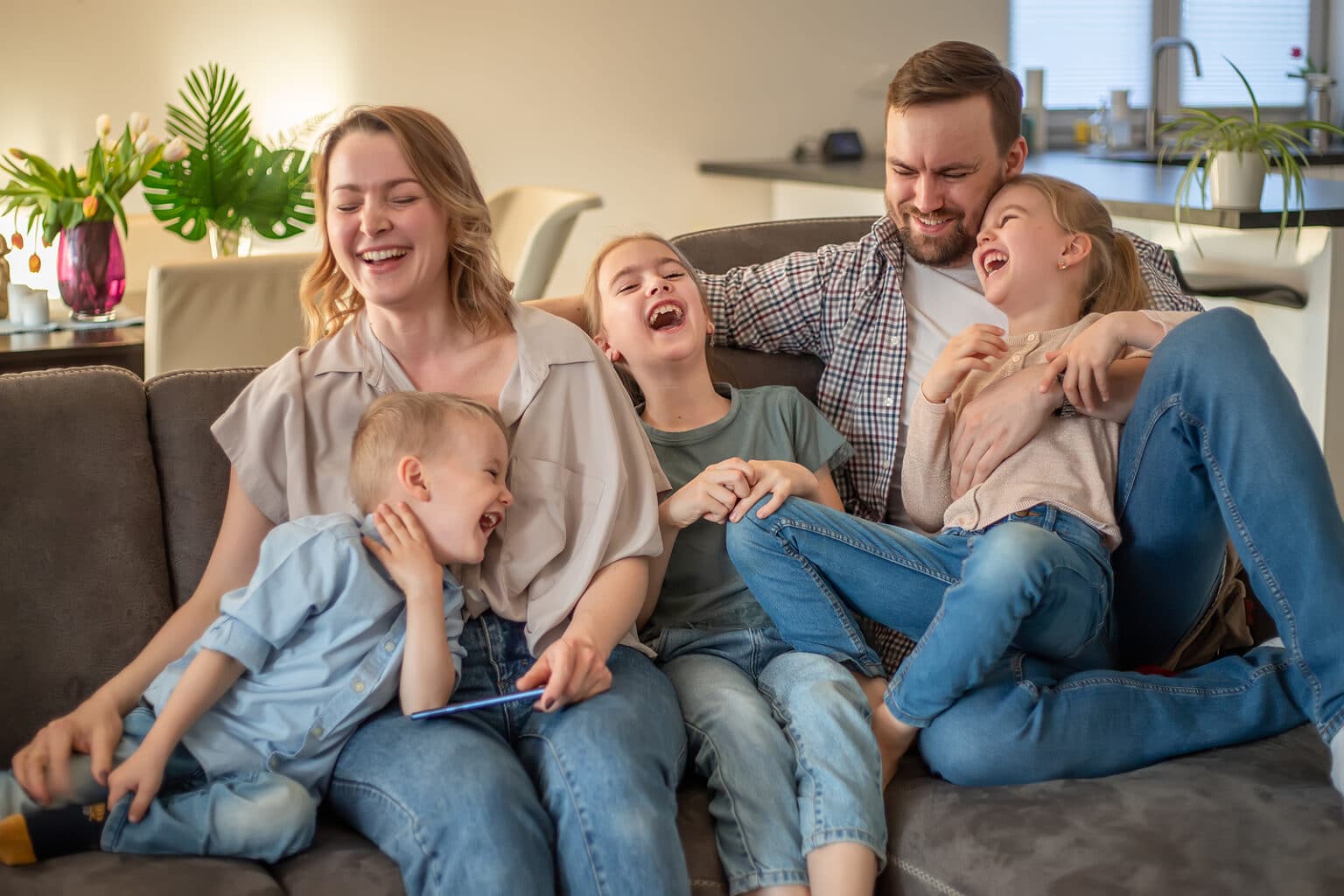 A young family with three children laughing together on the couch at home